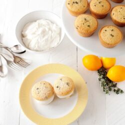 Delicious lemon blueberry muffins on a white plate with whipped cream and fresh lemons.