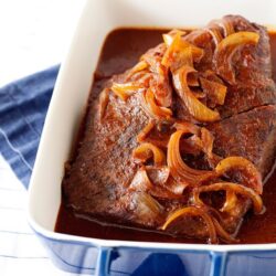 Slow cooker beef roast with caramelized onions and rich gravy in a white and blue ceramic dish.