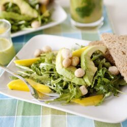 Fresh green salad with avocado, chickpeas, and whole wheat bread slices on a white plate.