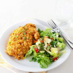Golden fried chicken breast served with fresh garden salad on white plate.