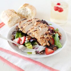 Grilled chicken salad with fresh strawberries and mixed greens on a white plate.