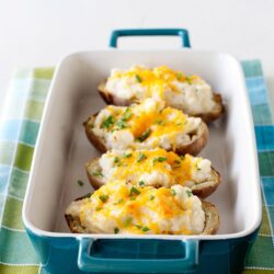 Baked potato halves topped with scrambled eggs, cheese, and chives in a baking dish.