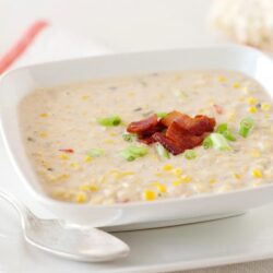 Creamy corn chowder with bacon and green onions in a white bowl, served with bread.