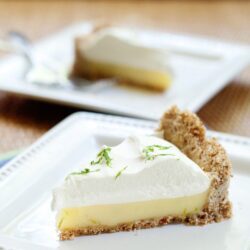 Cream cheese pie with graham cracker crust topped with whipped cream and lime zest, served on a white plate.