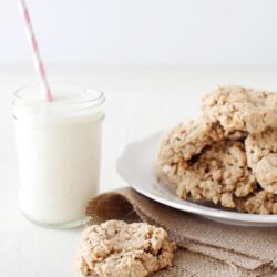 Flaky homemade oatmeal cookies served with glass of milk on white table.
