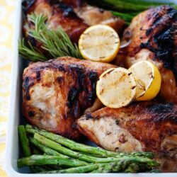 Roasted chicken with lemon, asparagus, and herbs in a white baking dish.