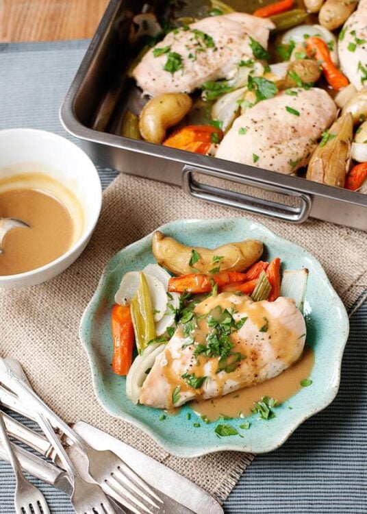 Juicy baked chicken breast with roasted vegetables and herb gravy on a rustic plate.