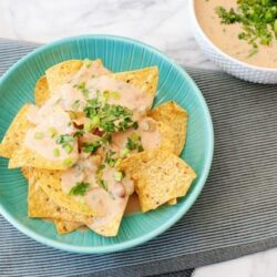 Creamy taco dip with crispy tortilla chips on a turquoise plate. Perfect appetizer for parties and gatherings.