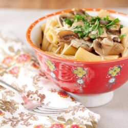 Creamy mushroom and pasta in a red floral bowl on a decorative napkin.