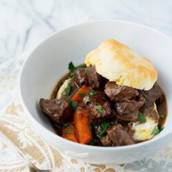 Hearty beef stew with carrots and mashed potato topping in a white bowl.