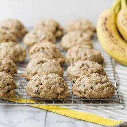 Oatmeal banana cookies cooling on a wire rack with bananas in the background.