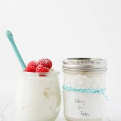 Creamy white fudge topped with fresh raspberries in a glass jar.