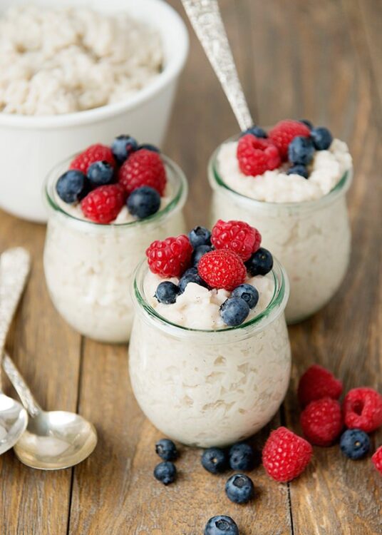 Creamy cottage cheese parfait with fresh raspberries and blueberries in glass jars, on rustic wooden table.