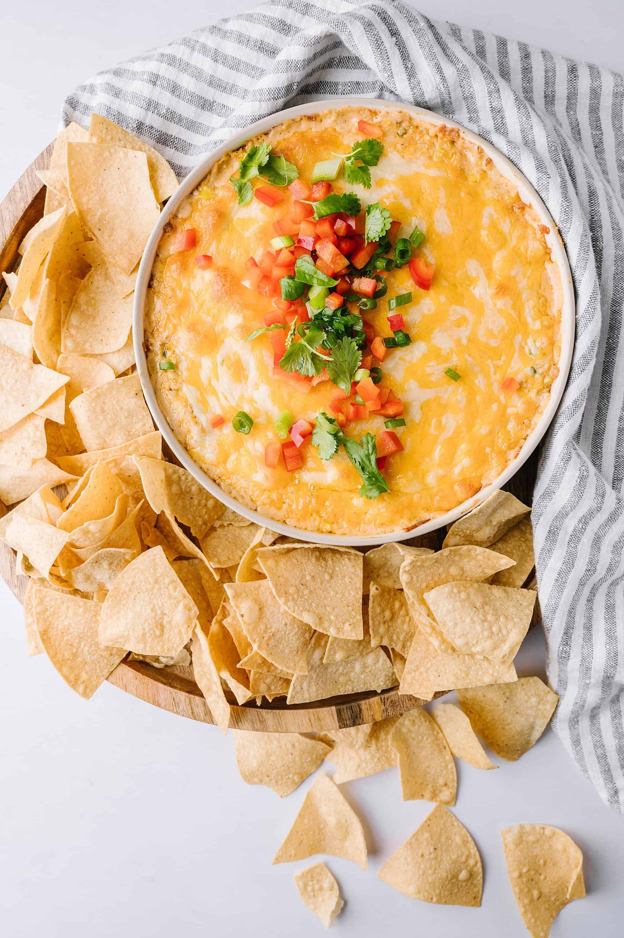 Creamy baked queso dip garnished with tomatoes, green onions, and cilantro served with tortilla chips.
