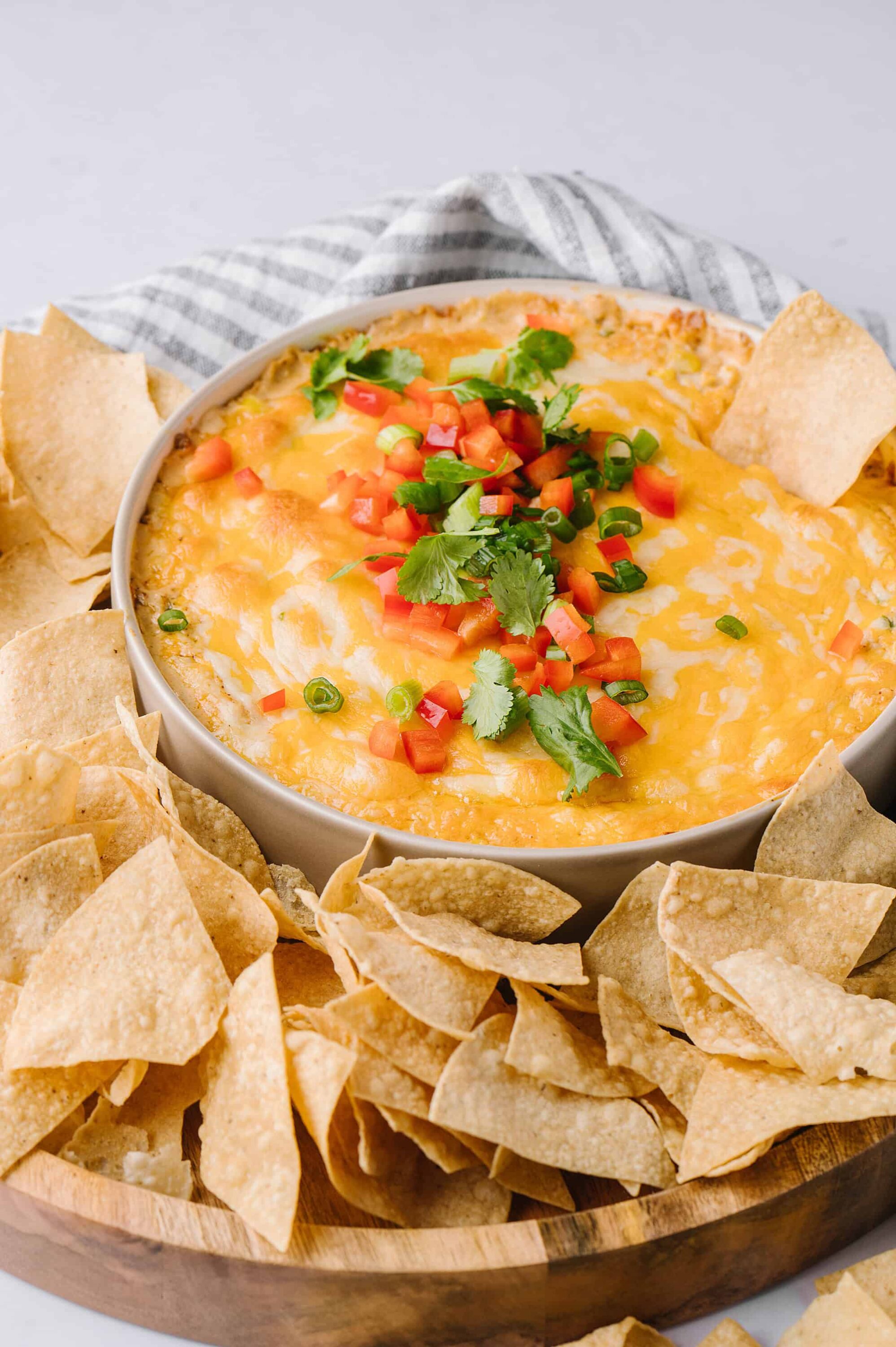 Cheesy baked dip garnished with fresh cilantro and diced tomatoes, served with crispy tortilla chips.