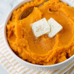 Creamy pumpkin mashed potatoes with butter, served in a white bowl with a silver spoon.