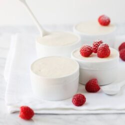 Fresh creamy raspberry sauce in white bowls with ripe raspberries and a white spoon on a white cloth.