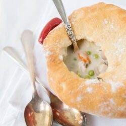 Creamy chicken pot pie soup served in a bread bowl, fresh homemade bread with vegetables and hearty filling.