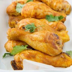 Golden baked chicken drumsticks with fresh cilantro on a white plate.