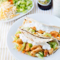 Crispy chicken tacos with fresh vegetables and creamy sauce on white plate.