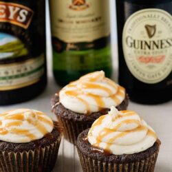 Rich chocolate cupcakes with creamy frosting and caramel drizzle, surrounded by beer bottles, perfect for indulgent dessert recipes.