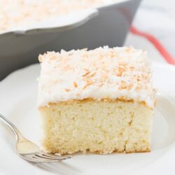 Fluffy coconut cake slice with white frosting and toasted coconut topping.