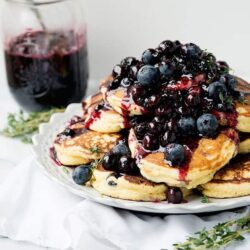 Fluffy blueberry pancakes topped with fresh berries and syrup on a white plate.
