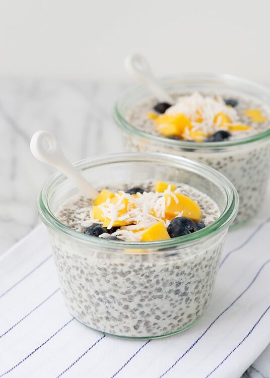 Creamy chia seed pudding with fresh blueberries, mango chunks, and shredded coconut in glass bowls.