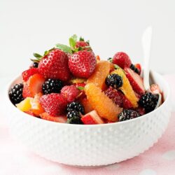 Fresh fruit salad with strawberries, blackberries, oranges, and other seasonal fruit in a white bowl.