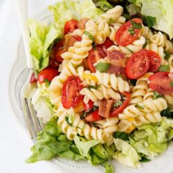 Fresh pasta salad with cherry tomatoes, bacon, and green onions on a white plate.
