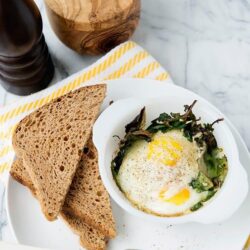 Scrambled eggs with greens served with whole wheat toast on a white plate.
