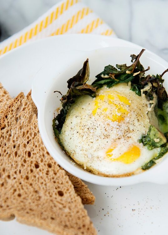 Cream-poached eggs with wilted greens on white plate with toasted bread slices.
