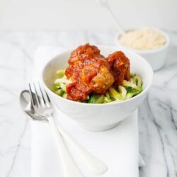 Savory chicken meatballs with zucchini noodles and marinara sauce on white bowl.