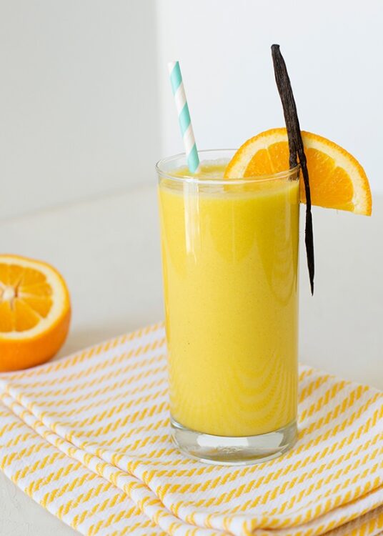 Fresh orange vanilla smoothie garnished with orange slices and a vanilla bean, served with a striped straw.