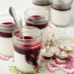 Creamy yogurt dessert with mixed berry compote in glass jars, on a floral tablecloth.