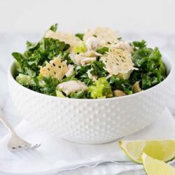 Fresh Caesar salad with parmesan cheese and lemon wedges on marble table, healthy homemade salad recipe.