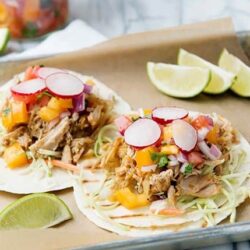 Shredded pork tacos with fresh radishes and lime wedges on a parchment-lined tray.