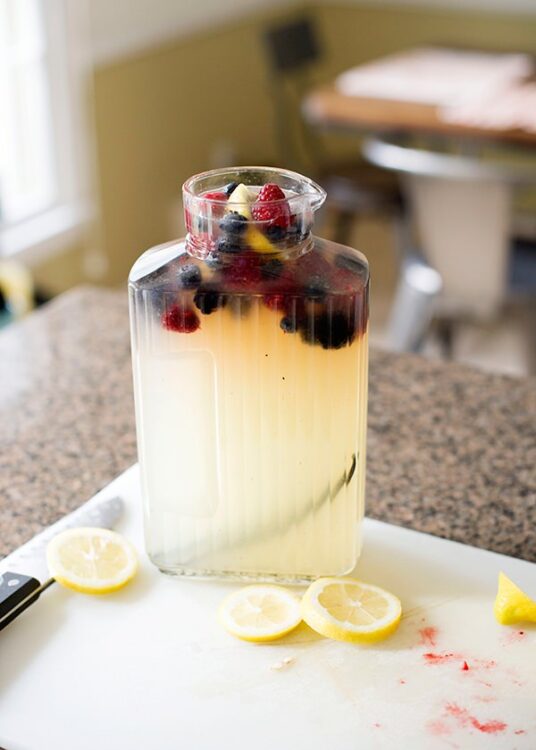 Fresh fruit-infused water with berries and lemon slices in a glass jar, on a kitchen countertop.