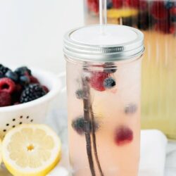 Refreshing berry infused lemonade in a mason jar with a straw, with fresh berries and lemon slices for garnish.