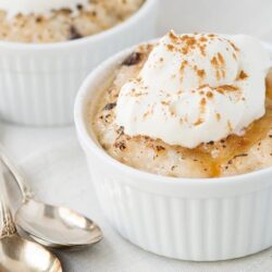 Creamy apple crisp topped with whipped cream in a white ramekin, perfect for fall desserts.