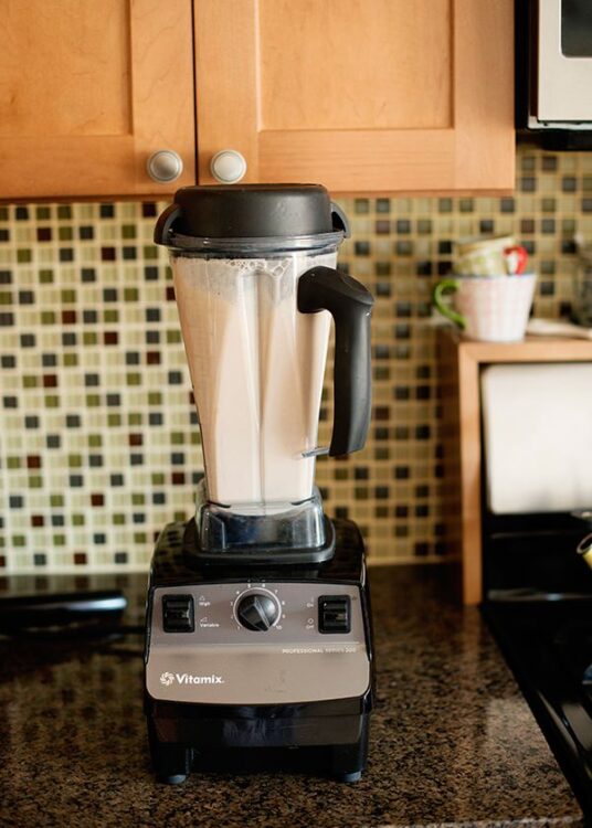 Blender with creamy smoothie on a kitchen countertop, Vitamix appliance, modern kitchen setting, healthy drink preparation.