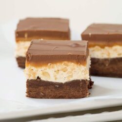 Rich layered dessert bars with chocolate, caramel, and crispy rice on a white plate.