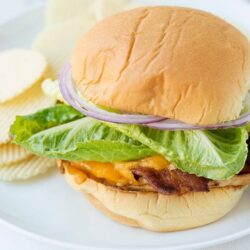 Crispy cheeseburger with lettuce and onions on soft bun, baked bree recipe.