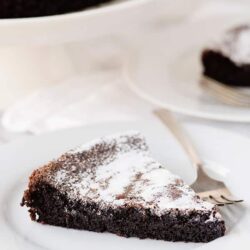 Decadent Chocolate Cake Slice with Powdered Sugar on White Plate.