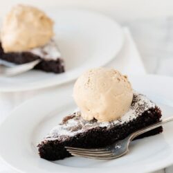 Rich chocolate cake slice with vanilla ice cream on white plate.