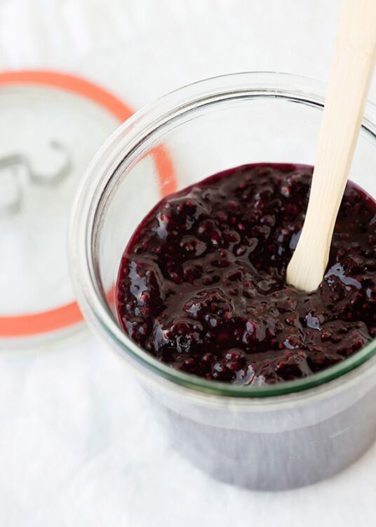 Sweet black berry jam in a glass jar with a wooden spoon, perfect for baking and spreading.