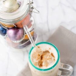 Colorful Christmas baubles in a glass jar with a milkshake on marble; holiday decoration and festive drink.