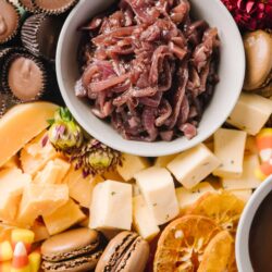 Crispy bacon and cheese charcuterie board with chocolate candies, macarons, and dried orange slices.