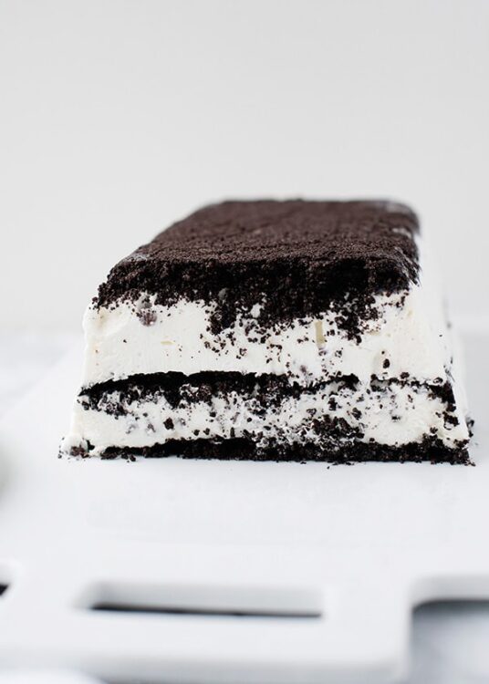 Creamy cookies and cream ice cream bar with Oreo cookie crumbs, on a white surface.