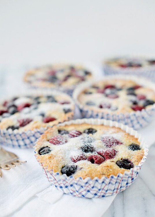 Fresh berry muffins in paper liners on white cloth, baked by Baked Bree.